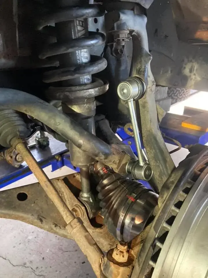 A close-up of a 4WD's front suspension, CV joint and sway bar link under the hoist